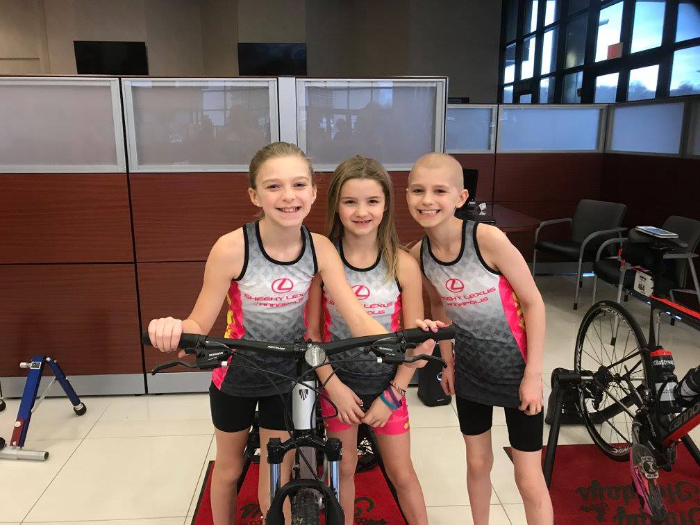 Ella and two friends in cycling jerseys at an indoor spin-a-thon fundraiser