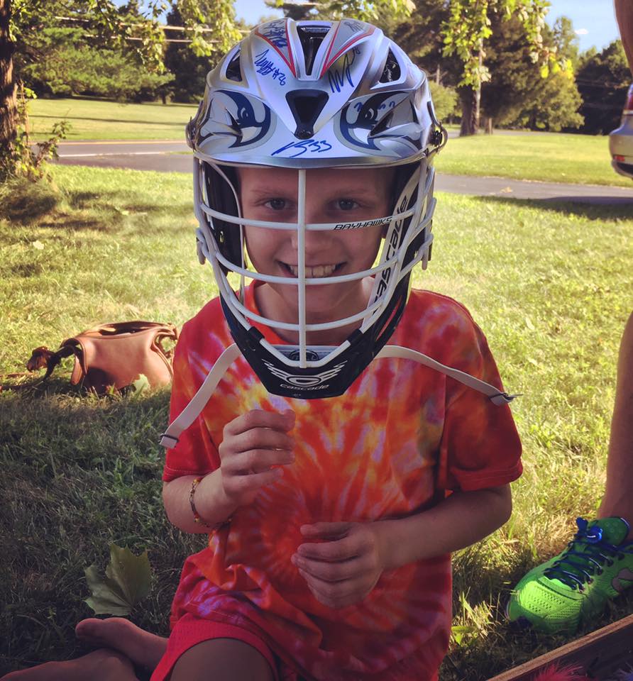 Ella grinning inside an oversized signed lacrosse helmet