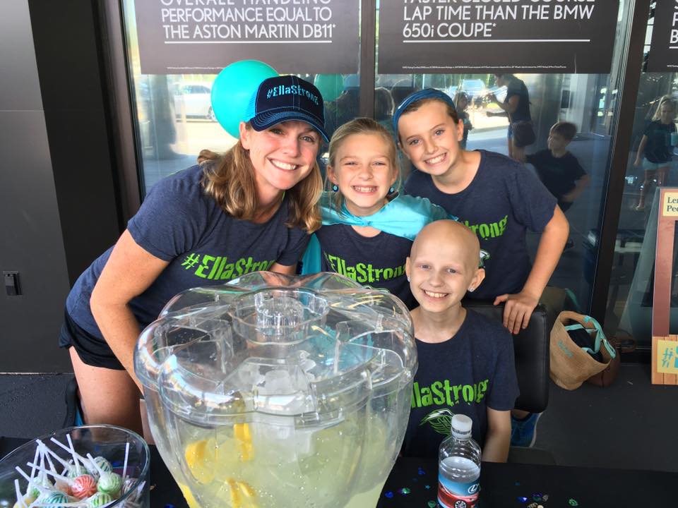 Ella, her mom and friends in #EllaStrong shirts behind a big jug of lemonade