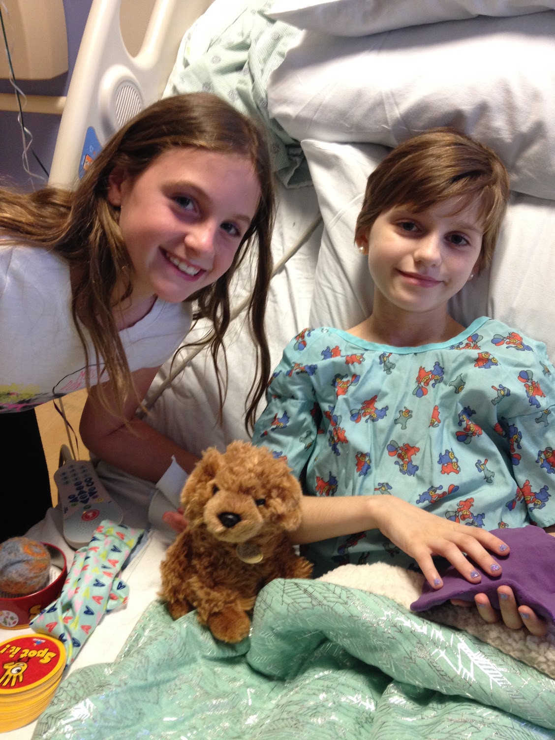 A friend leaning in beside Ella in her hospital bed with a stuffed puppy