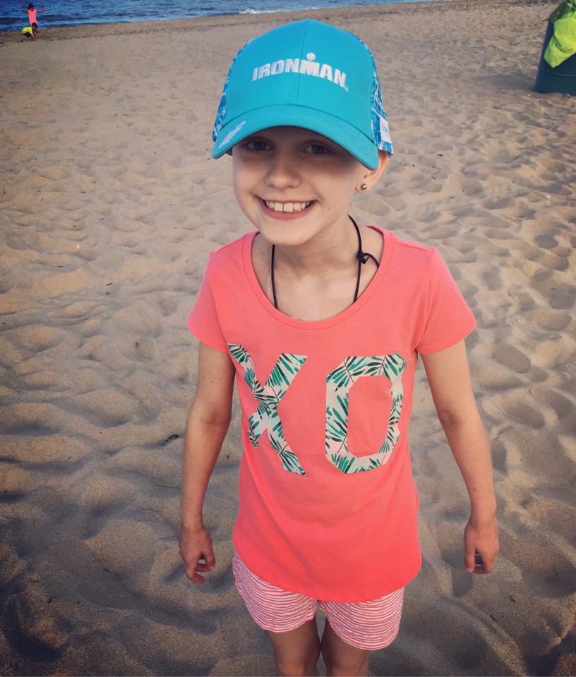 Ella smiling on the beach in an Ironman hat during treatment