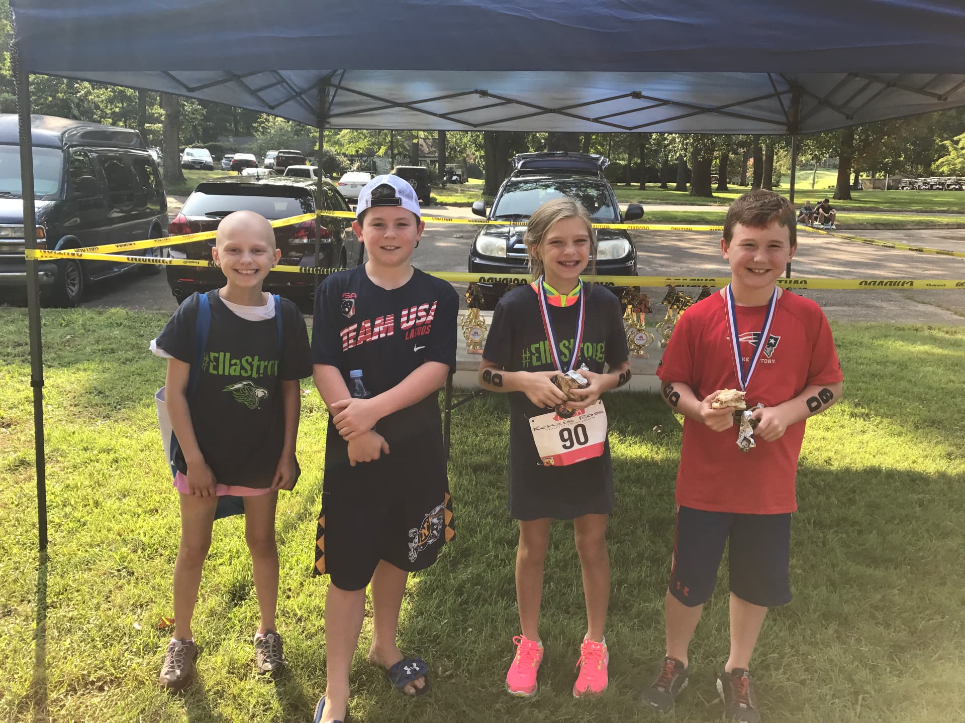 Ella and three friends with race medals under a tent at the youth triathlon