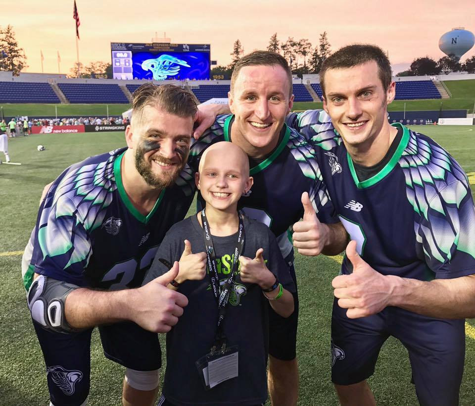 Ella giving two thumbs up with three Chesapeake Bayhawks lacrosse players on the field